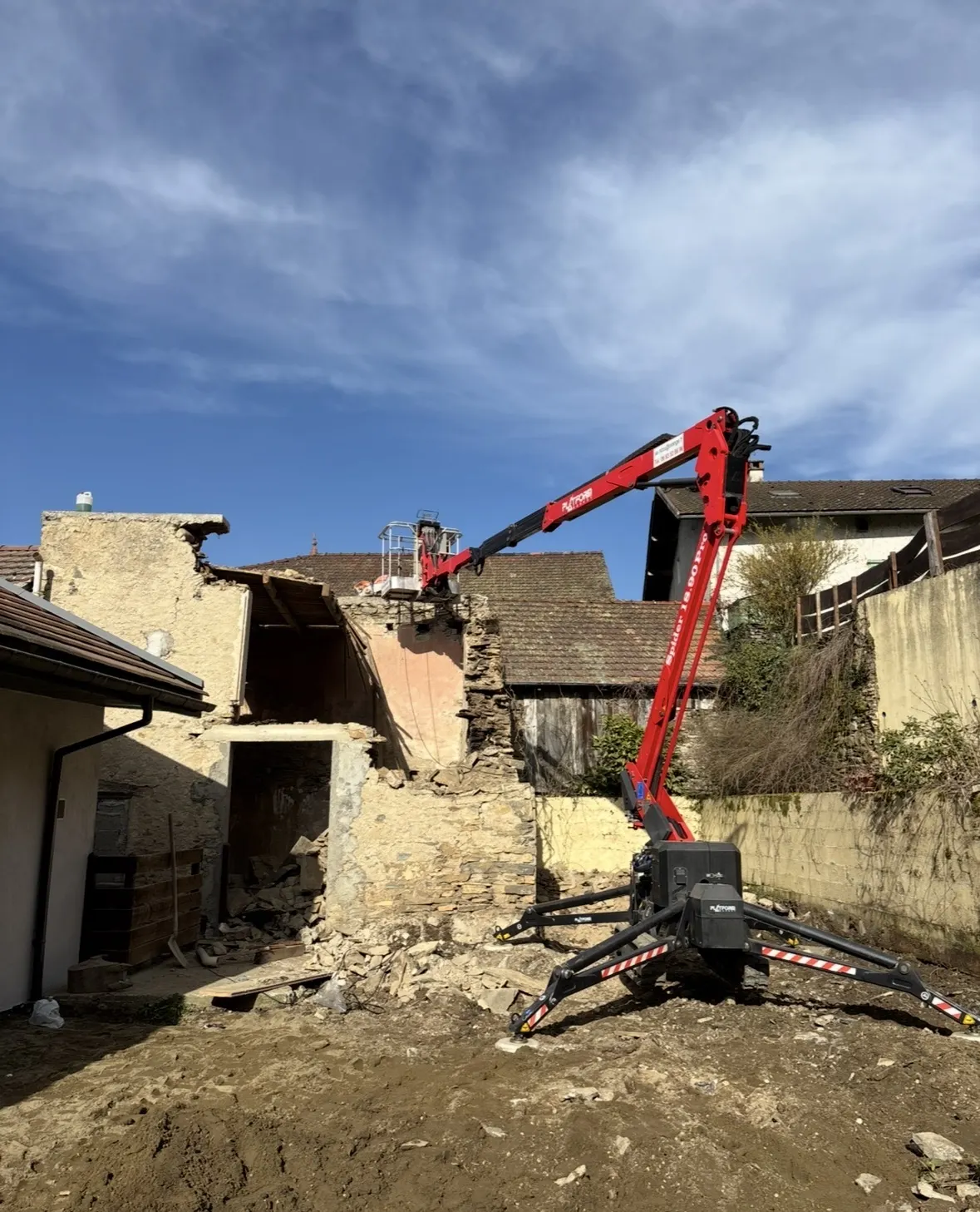 Démolition d'un bâtiment en pierre à la nacelle araignée, gravats amoncelés au pied du mur
